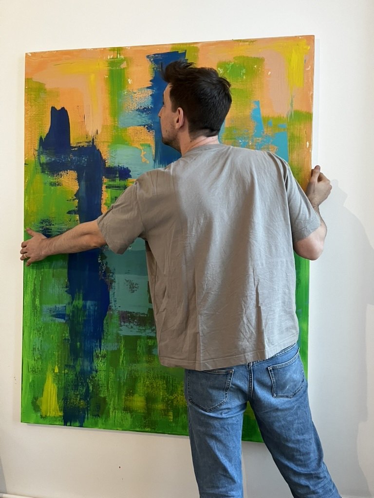 Der Künstler hängt eine großformatige Arbeit an eine weiße Wand