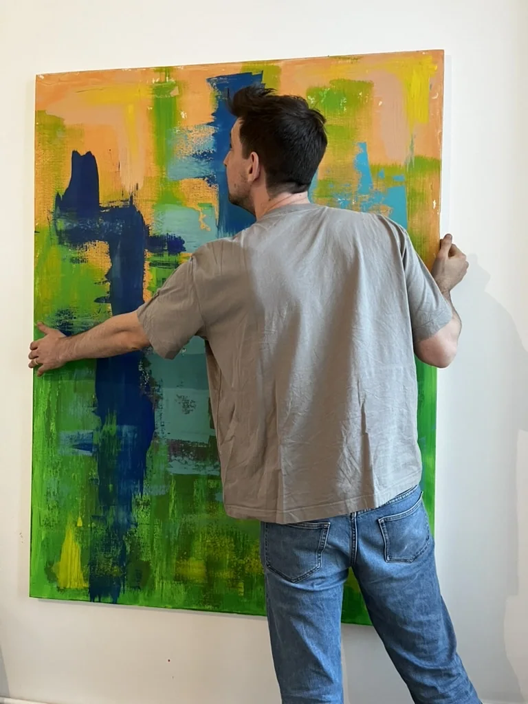 Der Künstler hängt eine großformatige Arbeit an eine weiße Wand